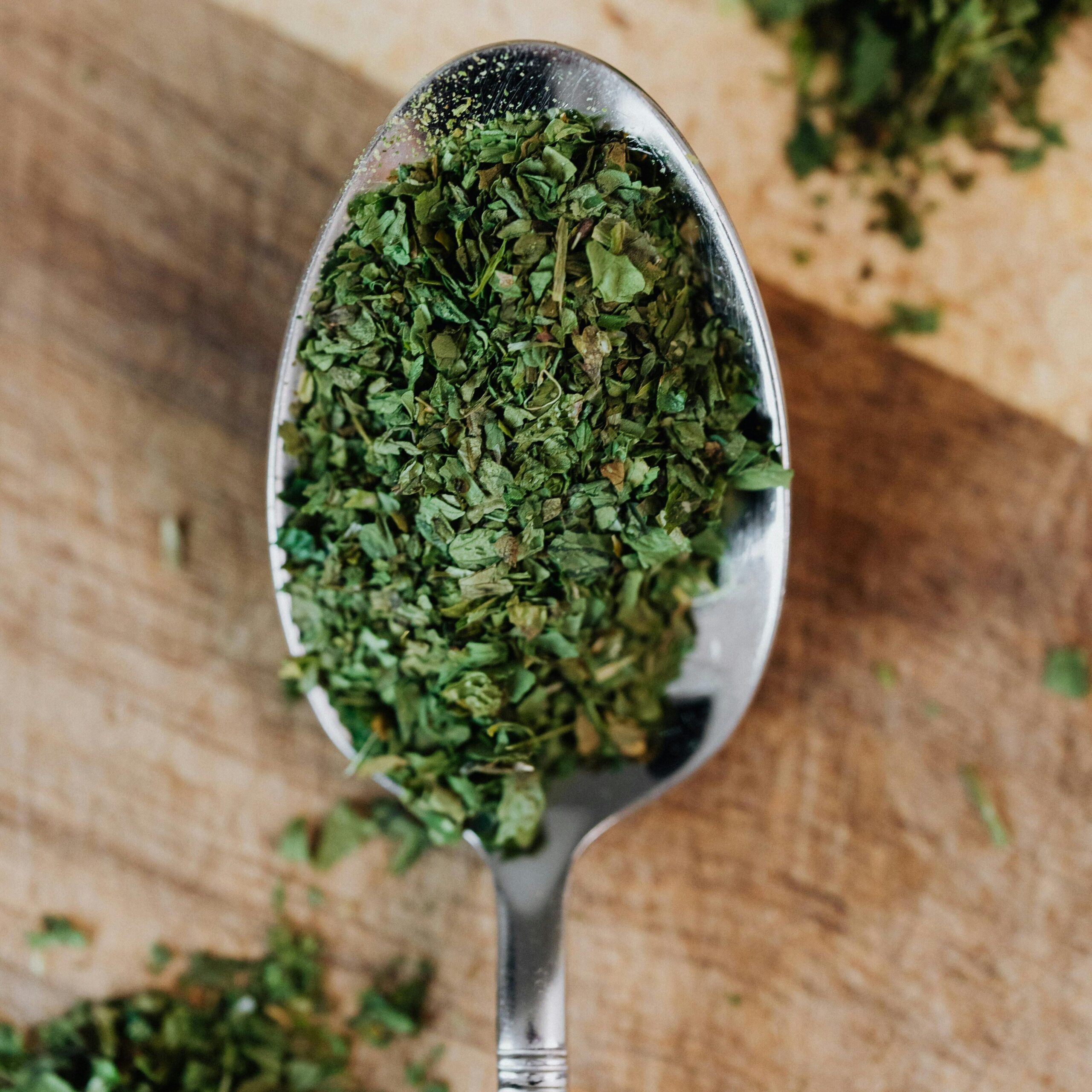 A detailed view of dried oregano herbs on a spoon over a wooden surface, showcasing freshness and texture.