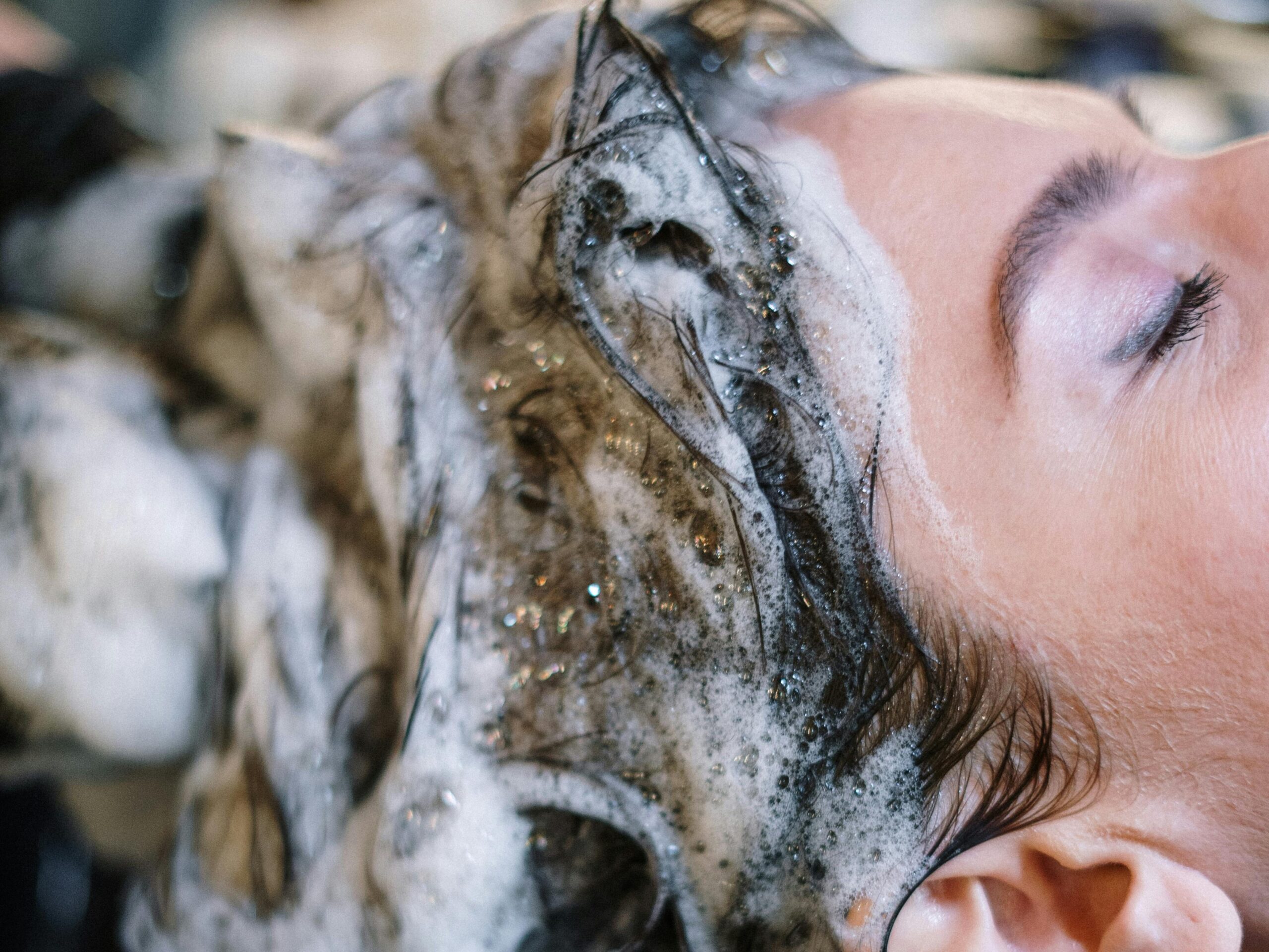 Woman enjoying a soothing hair wash with foamy shampoo at a salon sink.