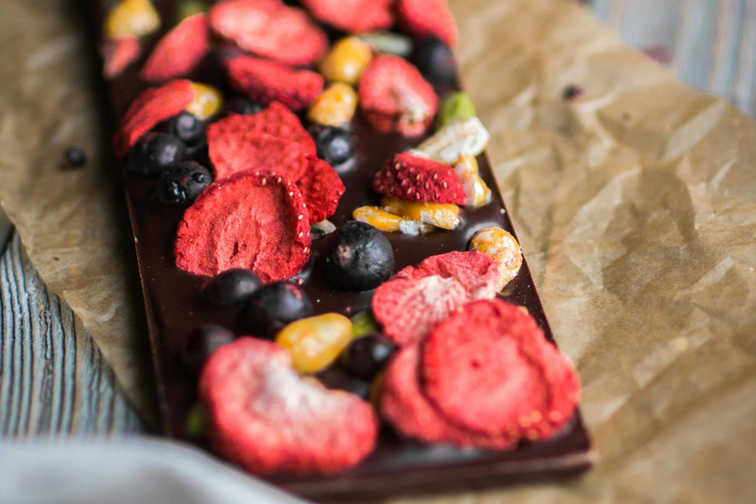 Artistic chocolate bar topped with dried berries and nuts on parchment paper.